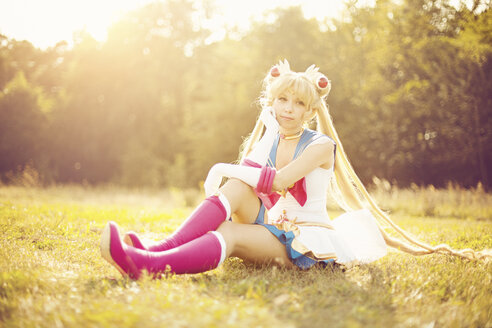 Woman wearing costume of Pretty Guardian Sailor Moon sitting on a meadow - AFF000100