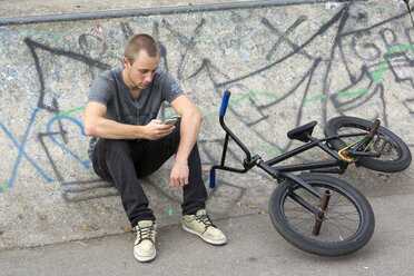 Junger Mann mit BMX-Rad, der sein Smartphone benutzt - DRF001142