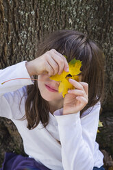 Portrait of girl peeking through hole in an autumn leaf - LVF002147