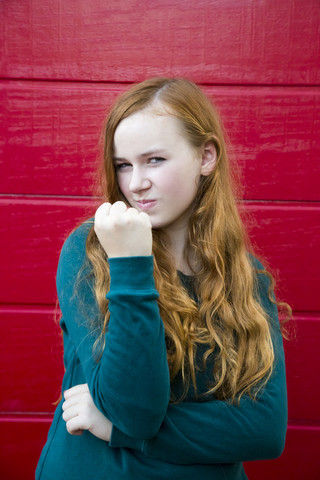 Portrait of teenage girl showing fist in front of red wooden wall stock photo