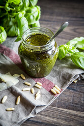 Ein Glas hausgemachtes Pesto Genovese, Pinienkerne, Basilikumblätter und Parmesan auf einem Küchenhandtuch - SARF000943