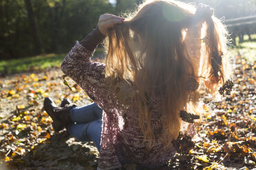 Teenager-Mädchen mit Herbstblättern im Haar sitzt im Gegenlicht - SARF000958