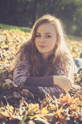 Portrait of teenage girl lying on the ground covered with autumn foliage - SARF000957