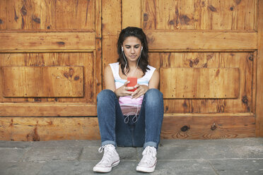Young woman hearing music with ear phones leaning at wooden door - EBSF000324