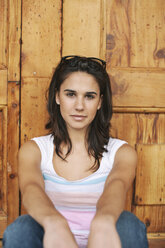 Porträt einer jungen Frau, die vor einer Holztür sitzt - EBSF000328