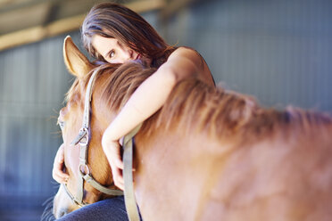 Teenage girl embracing horse in stable - ZEF001741
