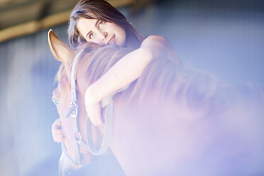 Teenage girl embracing horse in stable - ZEF001743