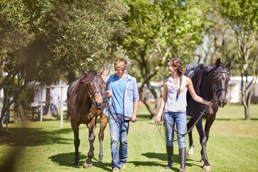 Junges Paar geht mit Pferden auf einer Wiese spazieren - ZEF001753