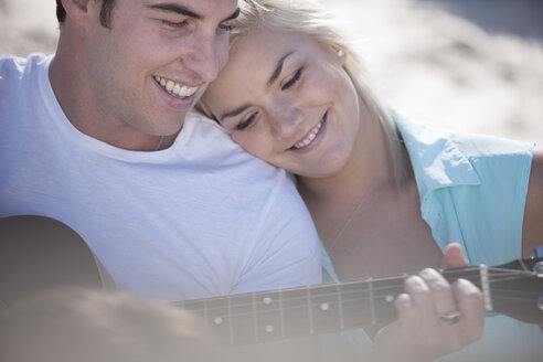 Junger Mann spielt Gitarre mit seiner Freundin am Strand - ZEF002444