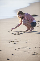 Junge Frau zeichnet Herz in Sand am Strand - ZEF002479