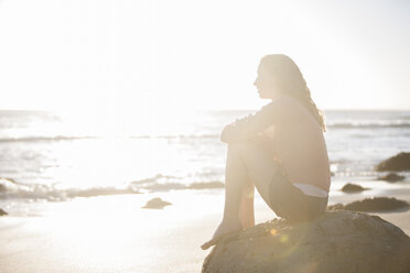 Junge Frau sitzt auf einem Felsen am Strand bei Sonnenuntergang - ZEF002482