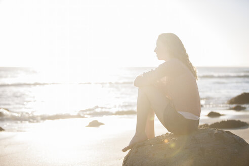 Young woman sitting on rock on the beach at sunset - ZEF002482