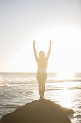 Junge Frau steht auf einem Felsen am Strand bei Sonnenuntergang - ZEF002483