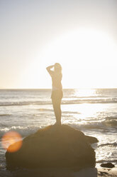 Young woman standing on rock on the beach at sunset - ZEF002484