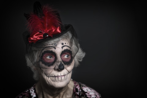 Porträt einer älteren Frau mit Zuckerschädel-Make-up und ausgefallenem Hut vor einem schwarzen Hintergrund, lizenzfreies Stockfoto
