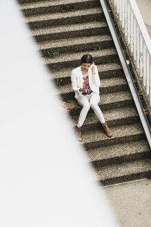 Junge Frau sitzt auf einer Treppe mit ihrem Smartphone, Blick von oben - UUF002339