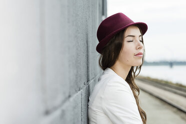 Portrait of young woman with closed eyes wearing hat leaning against a wall - UUF002345