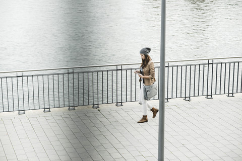 Junge Frau, die an der Promenade spazieren geht und sich mit einem digitalen Tablet orientiert, lizenzfreies Stockfoto