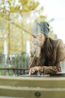 Junge Frau sitzt in einem Straßencafé und benutzt ein digitales Tablet - UUF002361