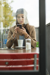 Junge Frau sitzt in einem Straßencafé und benutzt ihr Smartphone - UUF002363