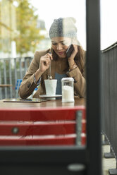 Junge Frau sitzt in einem Straßencafé und telefoniert mit ihrem Smartphone - UUF002364