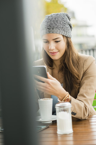 Lächelnde junge Frau sitzt in einem Straßencafé und liest SMS, lizenzfreies Stockfoto