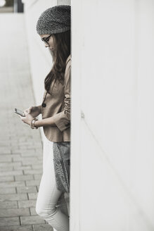 Junge Frau lehnt an einer Wand und liest SMS - UUF002464