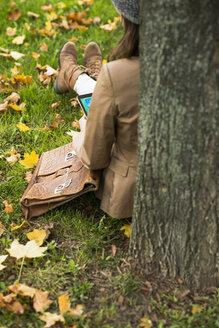 Junge Frau lehnt an einem Baum und benutzt ein digitales Tablet - UUF002380