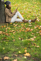 Young woman leaning against a tree using digital tablet - UUF002381