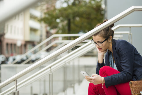 Junge Frau, die auf einer Treppe sitzt und SMS liest - UUF002395