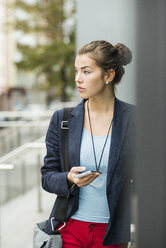 Young serious looking woman with smartphone waiting - UUF002398