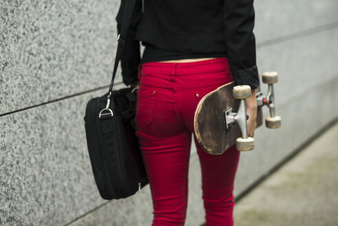 Junge Frau mit Tasche und Skateboard in roter Hose, Teilansicht - UUF002406