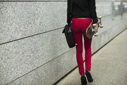 Junge Frau mit Tasche und Skateboard in roter Hose, Teilansicht - UUF002407