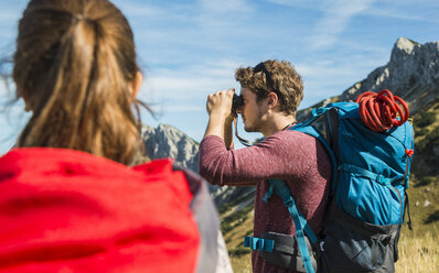 Austria, Tyrol, Tannheimer Tal, young man on hiking trip looking through binocular - UUF002435