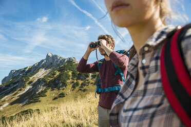 Österreich, Tirol, Tannheimer Tal, junger Mann auf Wandertour schaut durch ein Fernglas - UUF002436