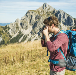 Austria, Tyrol, Tannheimer Tal, young man taking picture on alpine meadow - UUF002450