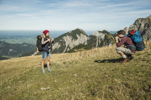 Österreich, Tirol, Tannheimer Tal, junger Mann fotografiert seine Freundin auf einer Almwiese, lizenzfreies Stockfoto