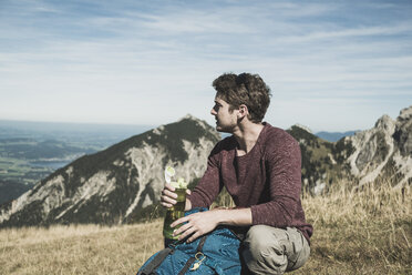Österreich, Tirol, Tannheimer Tal, junger Mann mit Rucksack und Trinkflasche auf Almwiese - UUF002457
