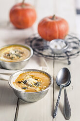 Schalen mit exotischer Kürbissuppe mit Kokosmilch und Kokosraspeln auf weißem Holz - SBDF001381