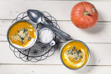 Two bowls of Exotic pumpkin soup with coconut milk and coconut flakes, spoons and pumpkin on white wood - SBDF001383