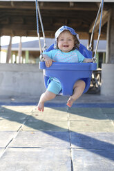 Lächelndes kleines Mädchen sitzt auf einer blauen Babyschaukel - SHKF000050