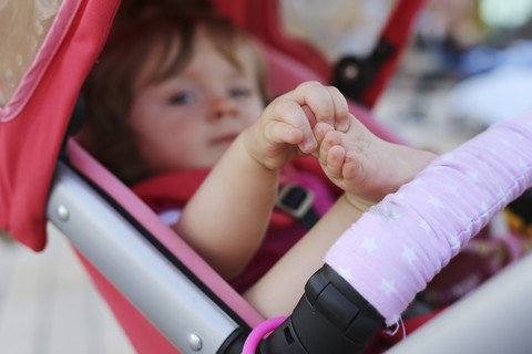 Kleines Mädchen im Kinderwagen spielt mit ihren Zehen, lizenzfreies Stockfoto