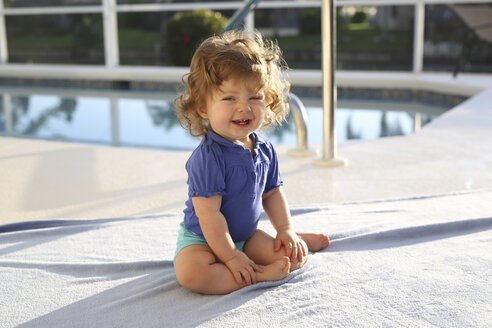 Porträt eines kleinen Mädchens, das auf einem Handtuch vor einem Schwimmbad sitzt - SHKF000059