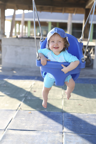 Lächelndes kleines Mädchen sitzt auf einer blauen Babyschaukel, lizenzfreies Stockfoto