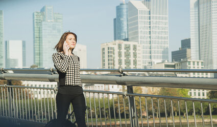 Germany, Frankfurt, young businesswoman on bridge on cell phone - UUF002471