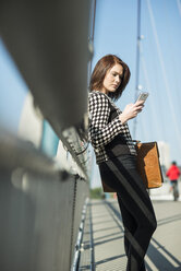 Deutschland, Frankfurt, junge Frau auf Brücke mit Mobiltelefon - UUF002475