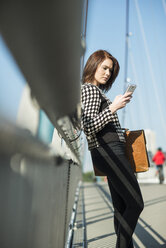 Germany, Frankfurt, young woman on bridge using cell phone - UUF002475