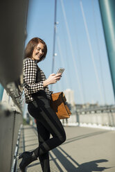 Deutschland, Frankfurt, junge Frau auf Brücke mit Mobiltelefon - UUF002476