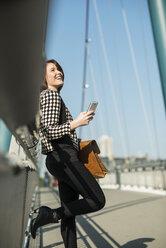 Germany, Frankfurt, young woman on bridge using cell phone - UUF002477