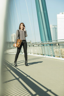 Deutschland, Frankfurt, junge Geschäftsfrau auf Brücke stehend mit Mobiltelefon - UUF002483